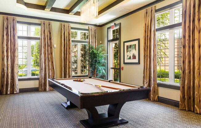 A pool table in a room with large windows and curtains.