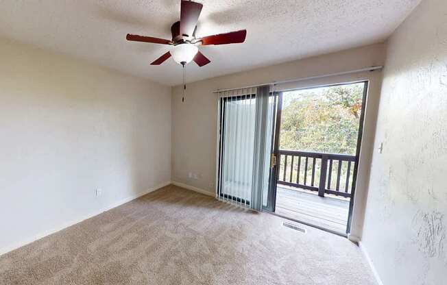 an empty living room with a ceiling fan and a balcony