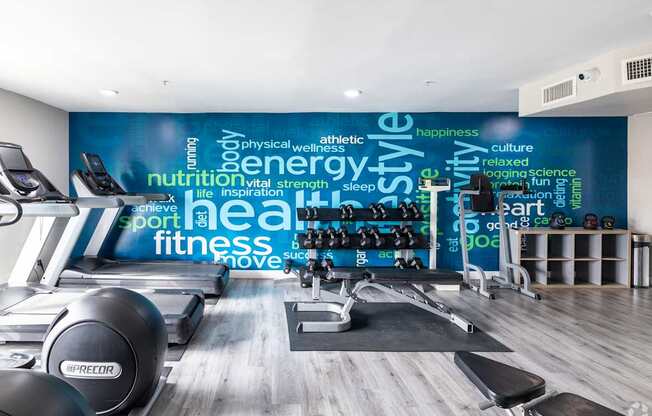 A gym with a variety of equipment and a wall with words related to fitness.