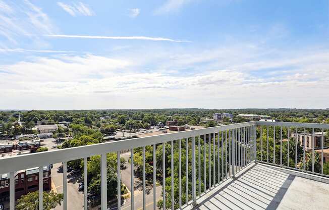 A balcony with a metal railing overlooks a parking lot and buildings.