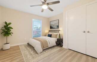 A bedroom with a bed, a ceiling fan, and a plant.