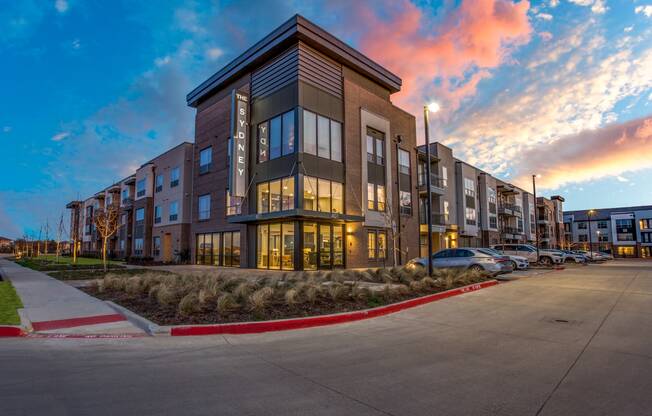 an apartment building at dusk with the sun setting behind it