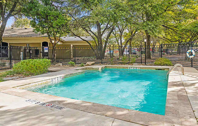 A small pool surrounded by trees and a fence.