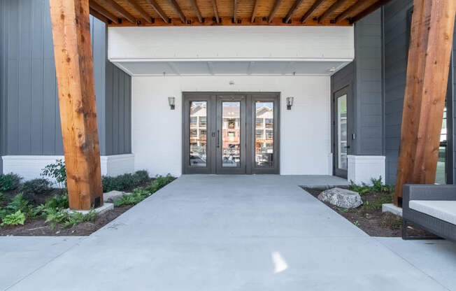 the front entrance of a building with a concrete walkway and wooden beams