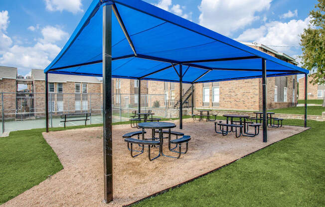 Fort Worth Apartments for Rent - Monarch Pass - Covered BBQ Area with Round Tables, Benches, and View of Sports Court and Apartment Buildings