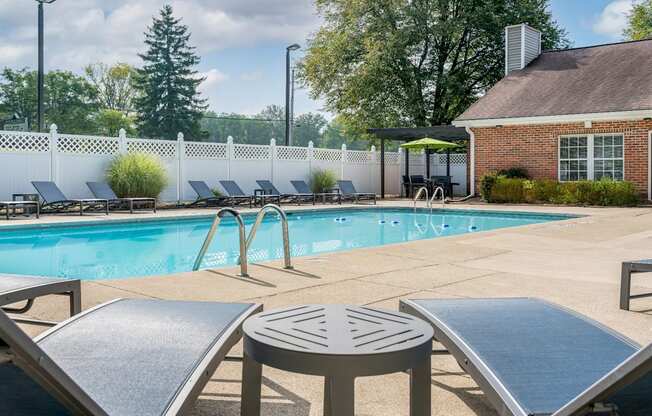 a swimming pool with lounge chairs and tables in front of a brick building with a white fence