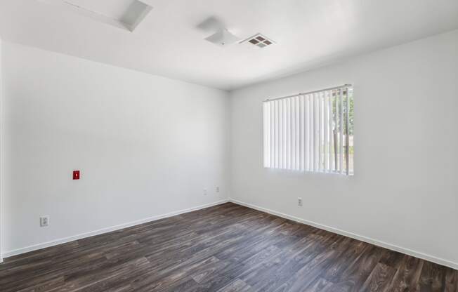 a bedroom with white walls and wood floors and a window