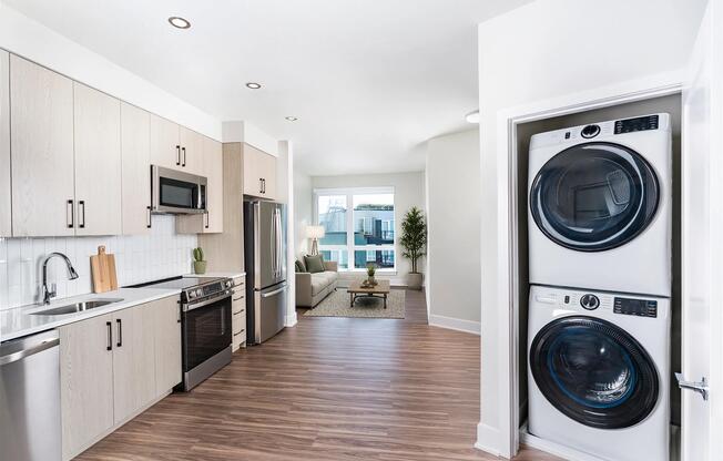 Open kitchen with quartz island seating, light wood cabinetry, and a dedicated in-home laundry closet positioned just outside the primary bedroom.
