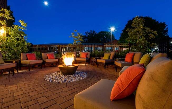 A fire pit in the middle of a patio surrounded by chairs and cushions.
