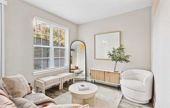 A living room with a white chair, a white sofa, a white coffee table, a white rug, a white wall, a white window with white blinds, a white floor, a white ceiling, a white picture frame, a white