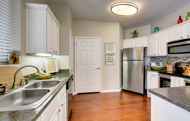 View of Upgraded Apartment Interior, Showing Kitchen with Plank Wood Flooring and Stainless Steel Appliances at Stonebriar of Frisco Apartments