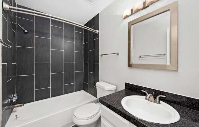 A bathroom with a black tiled shower area and a white toilet.