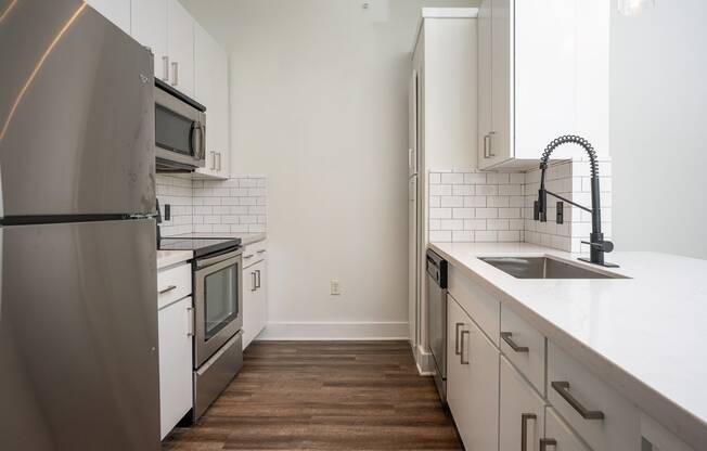 Dallas, TX, Apartments - Trend Design District - Kitchen with Faux-Wood Flooring, Stainless Steel Appliances, White Cabinetry, White Tile Backsplash, and Quartz Countertops.