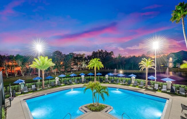 a swimming pool at night with palm trees and umbrellas