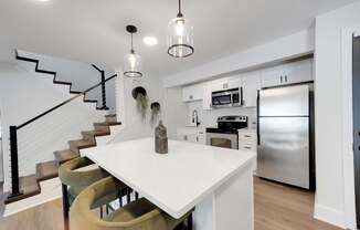 A modern kitchen with a white island and a staircase.