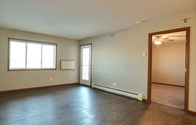 an empty living room with wood flooring and a window. Fargo, ND Urban Plains Apartments