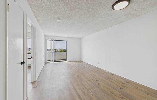 A room with a white ceiling and wooden flooring with a door on the left.