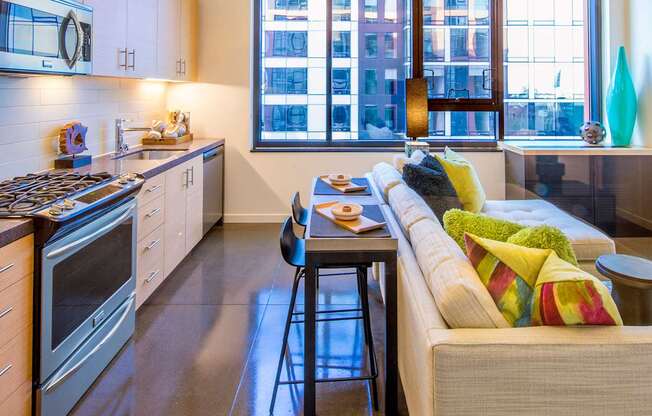 A modern kitchen with a bar stool and a couch with colorful pillows.