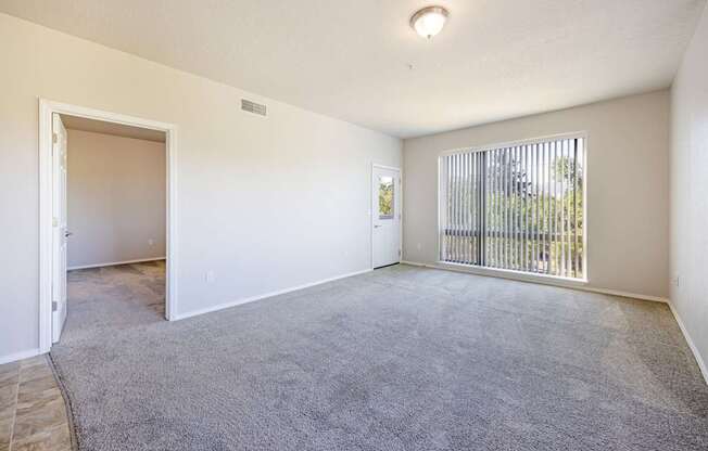 A room with a grey carpet and a window with a view of a fence.