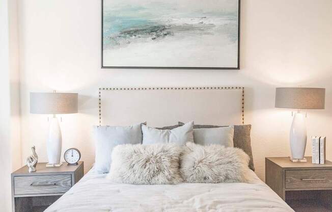 A bedroom with a large bed, two nightstands, and a painting on the wall.