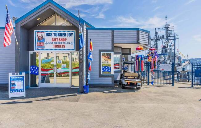 A gift shop named USS Turner Joy is located in front of a fence with flags at Spyglass Hill Apartments, Bremerton, 98337