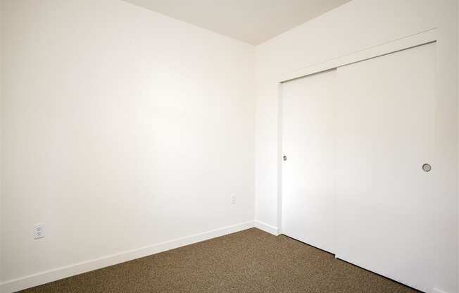 a bedroom with white walls and a door to a closet