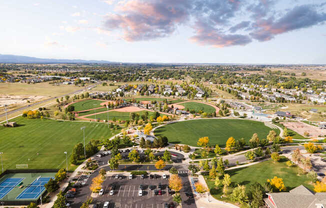 A park with a tennis court and a parking lot.