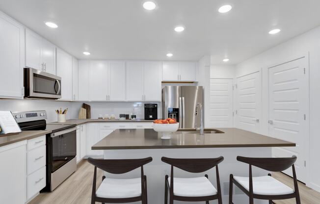 a kitchen with white cabinets and a large island with three chairs