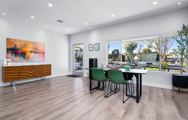 A room with a wooden floor, a table with chairs, and a large painting on the wall.