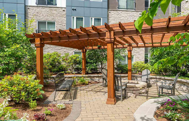 The Residences at Crosspoint central courtyard at 42 Wellman Street in Lowell, MA features paved walkways, raised garden beds, green shrubs, benches, and surrounding multi-story buildings clad in stone and metal siding.