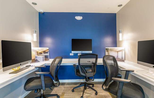 Three black chairs are positioned in front of two computer monitors in a room.