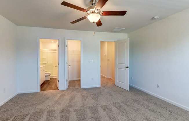 an empty living room with a ceiling fan and a door to a bathroom