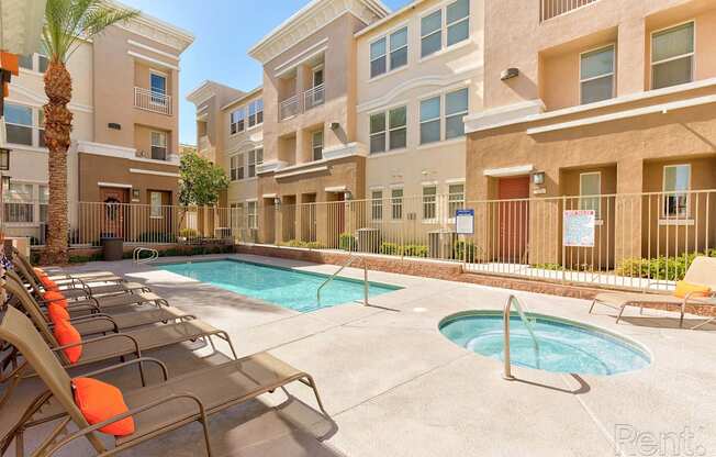 A pool area with sun loungers and a fence in front of apartment buildings.
