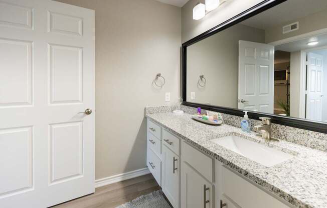 A bathroom with a white door and a sink with a mirror above it.