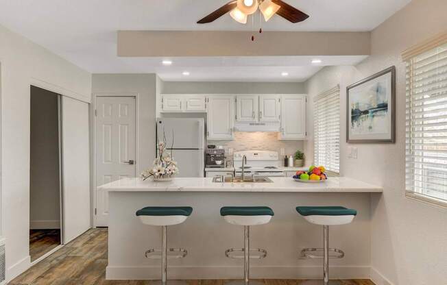 A kitchen with white cabinets and a white island with green bar stools.