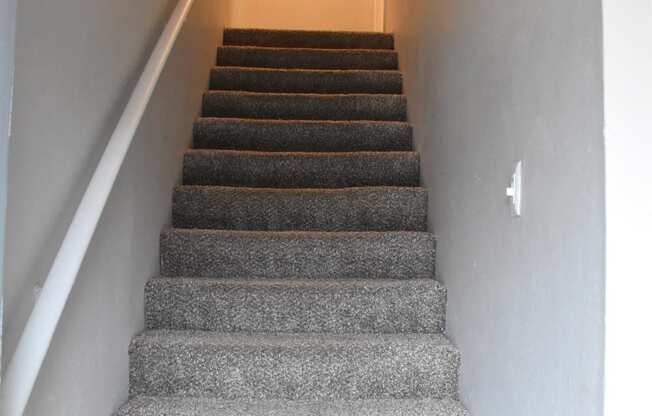 a flight of stairs leading up to a hallway with a white wall and a ceiling at Ivy Plains at Brooks Apartments, Texas