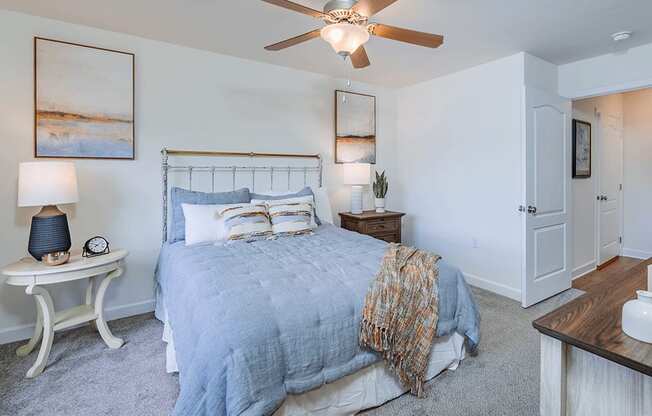 A bedroom with a bed, a fan, and a nightstand.