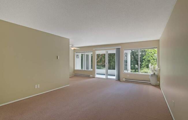 A spacious, empty living room here at Watercrest with soft carpet, large windows, and a sliding glass door leading to a private balcony, allowing abundant natural light and creating a bright, open atmosphere.