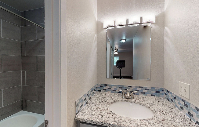 Modern bathroom with elegant granite countertop, stylish tile backsplash, and sleek lighting fixture.