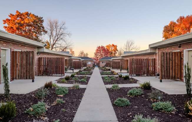 a pathway between two rows of brick buildings with plants and trees