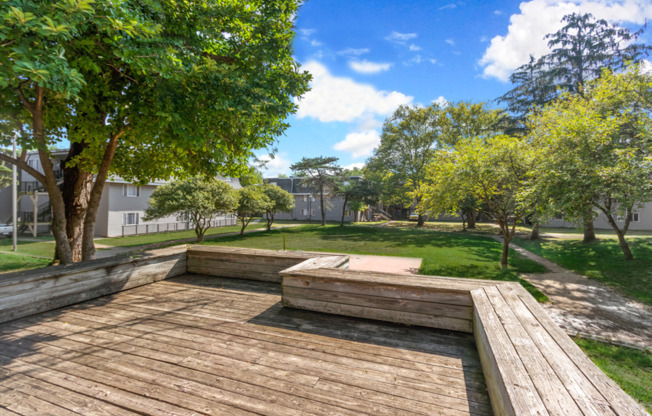 A wooden deck in a park with trees and a fence in the background.