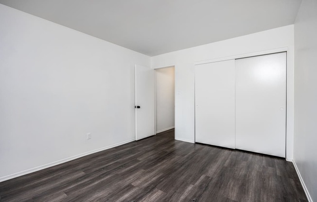 a bedroom with white walls and wood flooring and a closet