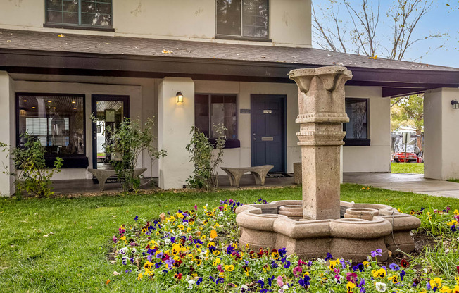a garden with a stone fountain in front of a house