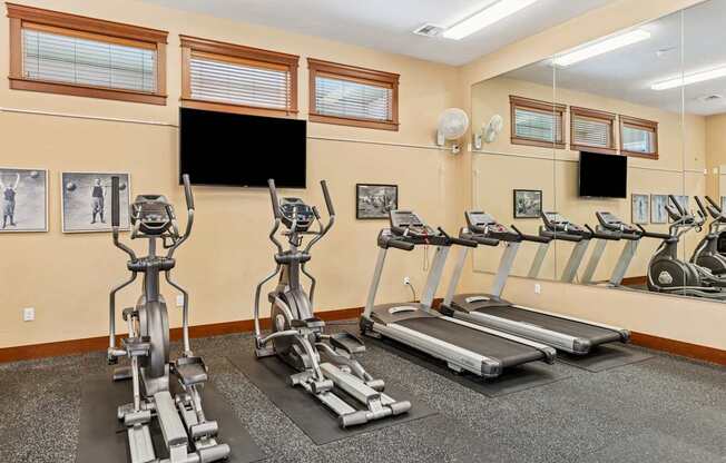 A gym with treadmills, elliptical machines, and a flat screen TV.