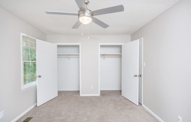 an empty room with a ceiling fan and two closets