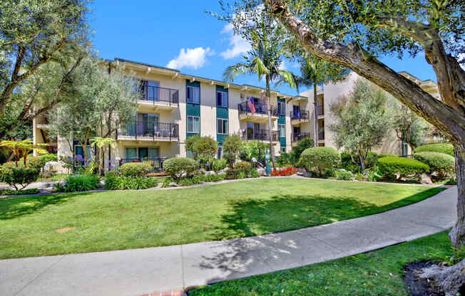 a sidewalk in front of an apartment building with grass and trees at Willow Tree Apartments, Torrance, CA