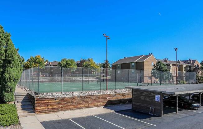 A tennis court surrounded by a fence and a parking lot.