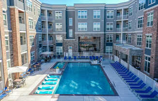 A large swimming pool surrounded by lounge chairs and umbrellas in a courtyard surrounded by apartment buildings.