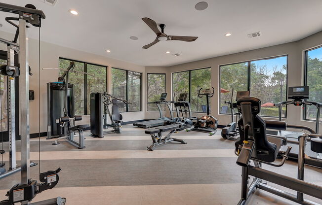 a gym with cardio equipment and windows in a home with a view of the woods