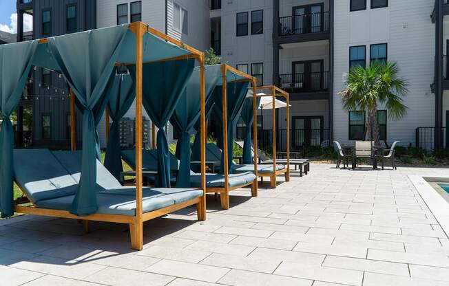 A row of wooden daybeds with green canopies are lined up on a patio.